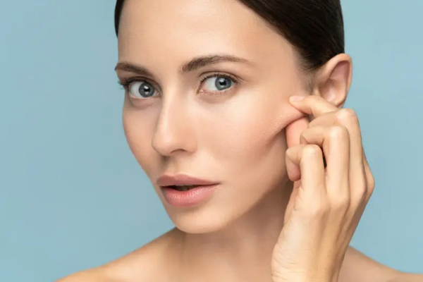 Woman touching the side of her face and illustrating loose or less firm skin